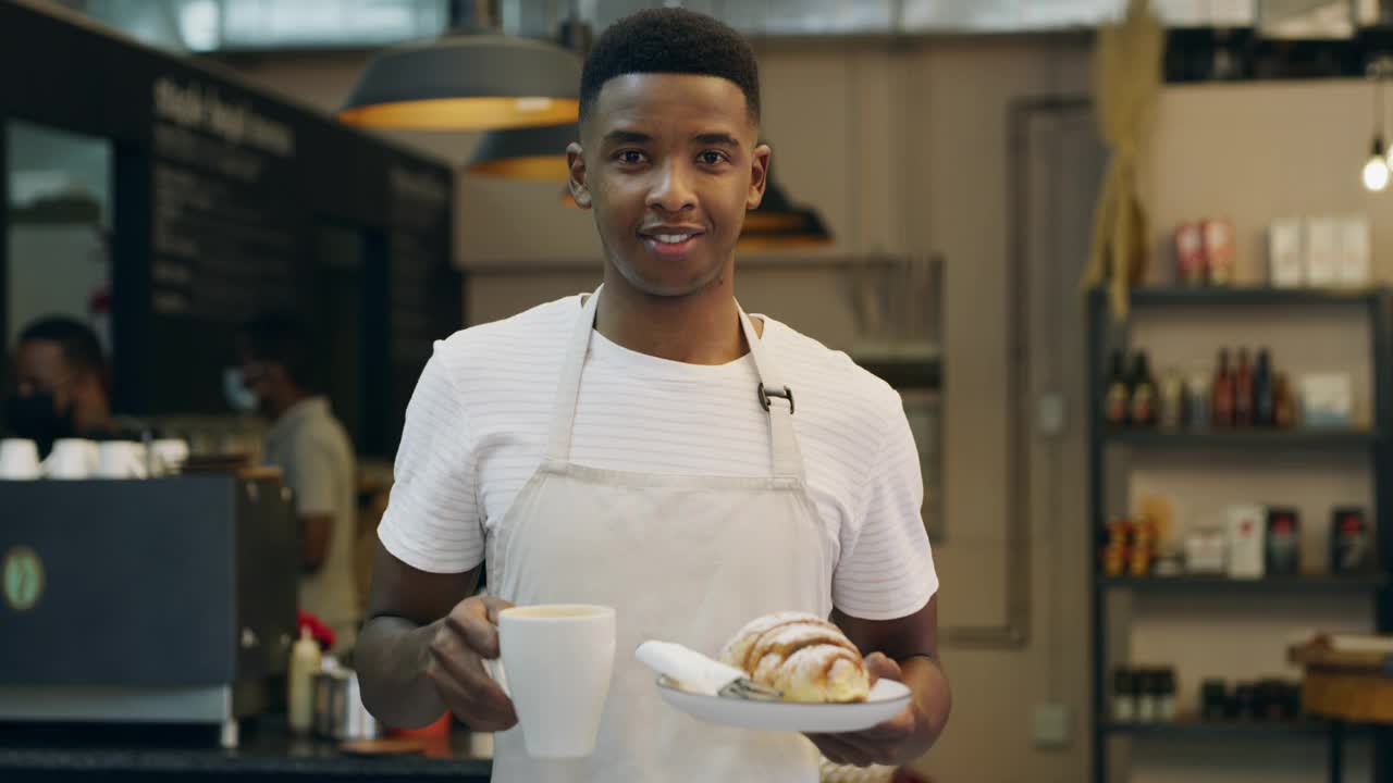 一段4k视频显示一名年轻的男面包师在面包房拿着一杯咖啡和一个盘子视频素材