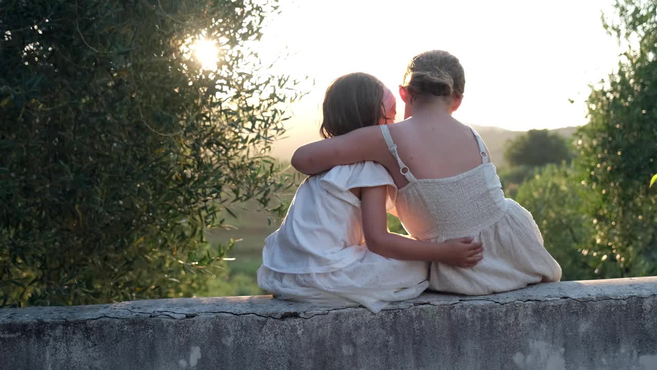 两个年轻的高加索姐妹花时间在一起聊天，拥抱和笑时坐在托斯卡纳别墅阳台墙在金色的阳光下午视频下载