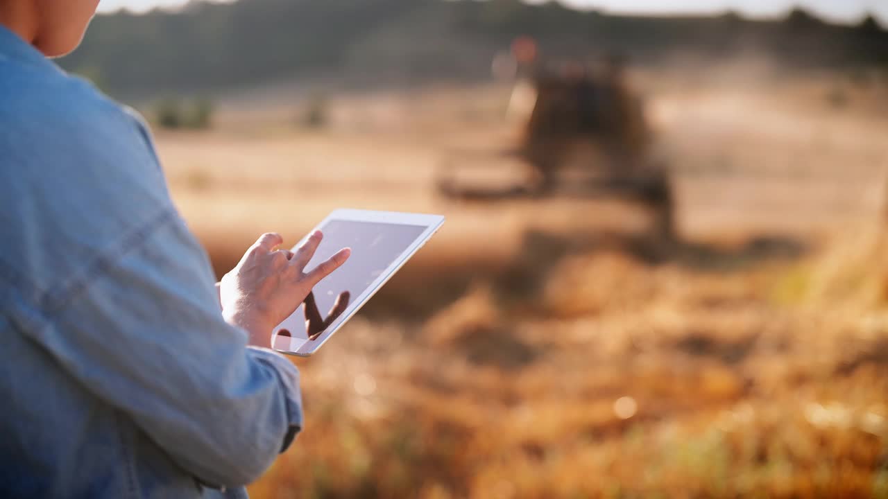 年轻的女农民使用数字平板电脑远程控制农场联合收割机视频下载