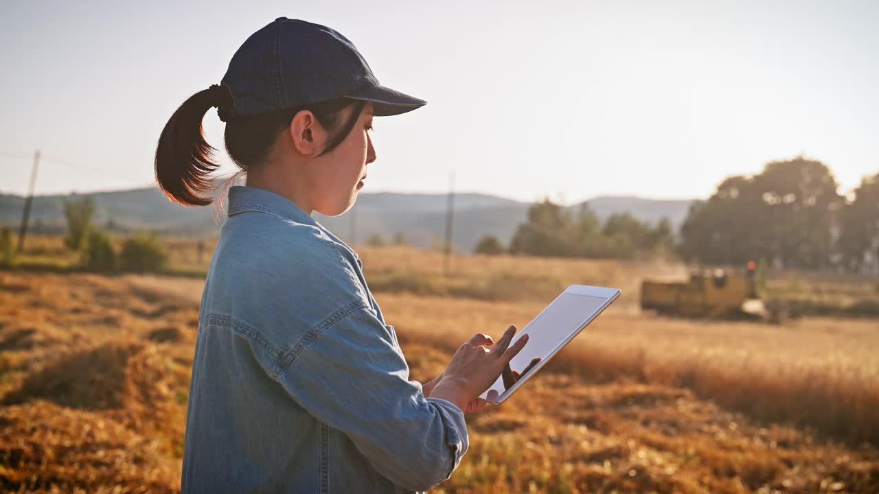 年轻的女农民使用数字平板电脑远程控制农场联合收割机视频素材