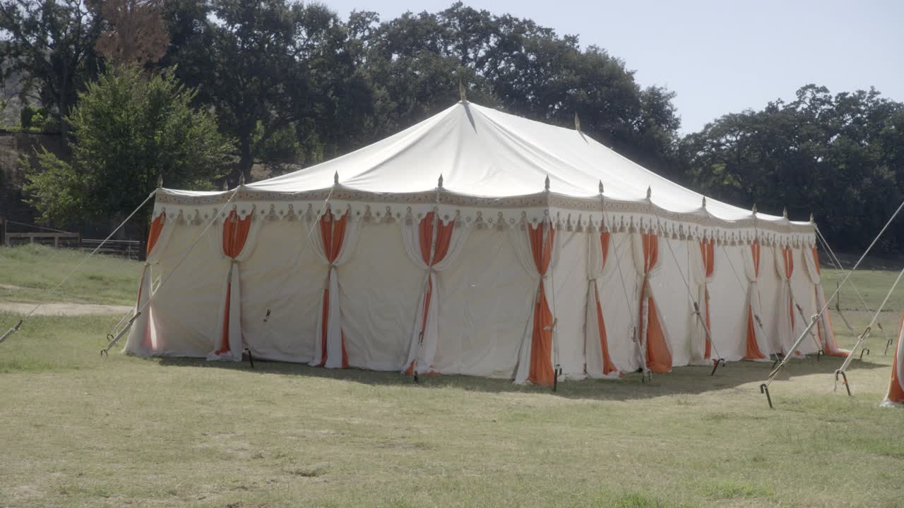 潘从左到右中等角度的两个白色和橙色马戏团帐篷在草坪或田野上可见。在bg中可见的树。可见写着“冥想”的木质标志。可以撤退。视频下载
