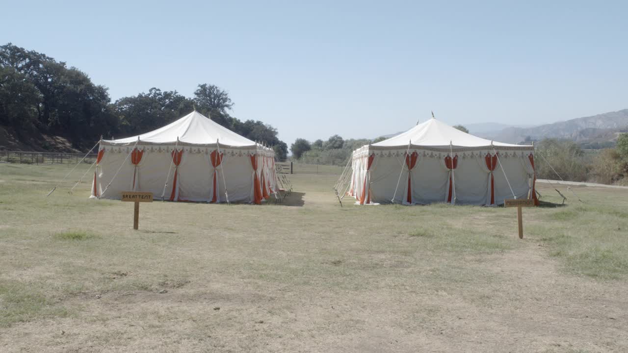 两个白色和橙色马戏团帐篷的广角可见草坪或田野。在bg可见的树木和山脉。可以撤退。可见两个木质标志。一个是“伟大的帐篷”，另一个是“冥想”。视频下载