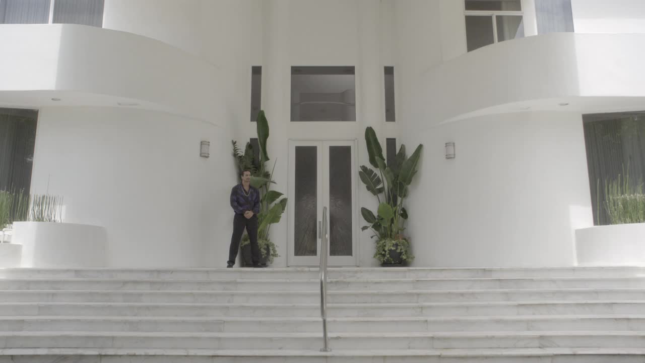 上层住宅、大厦或酒店门口站岗的男子的中等角度。楼梯可见。多层白色现代建筑。视频下载
