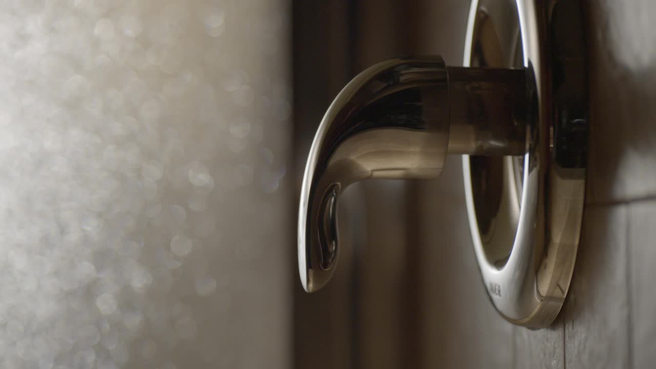 女人的手转动淋浴旋钮的闭合角度。淋浴间部分可见。视频素材