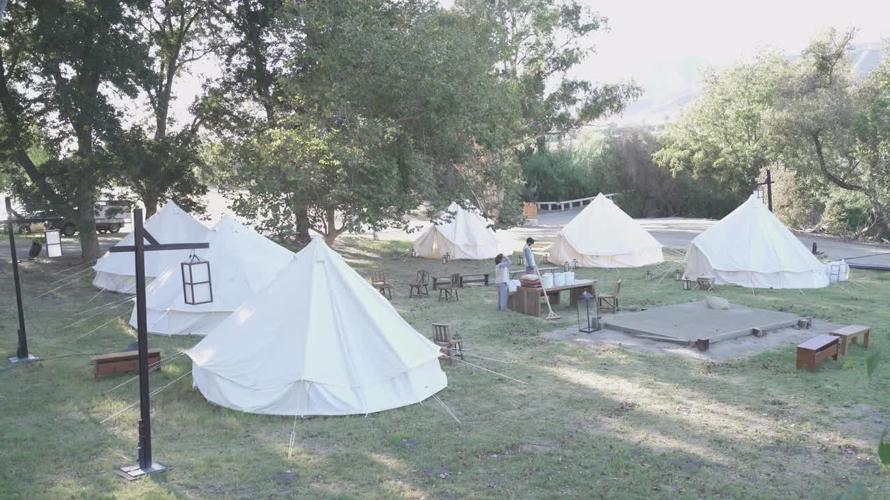 广角工人清理撤退或营地与蒙古包或帐篷，长凳和桌子在田野。视频下载