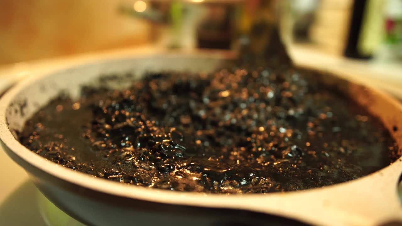 用锅铲在炉子上搅拌黑色调味饭。用米饭做黑烩饭。视频下载