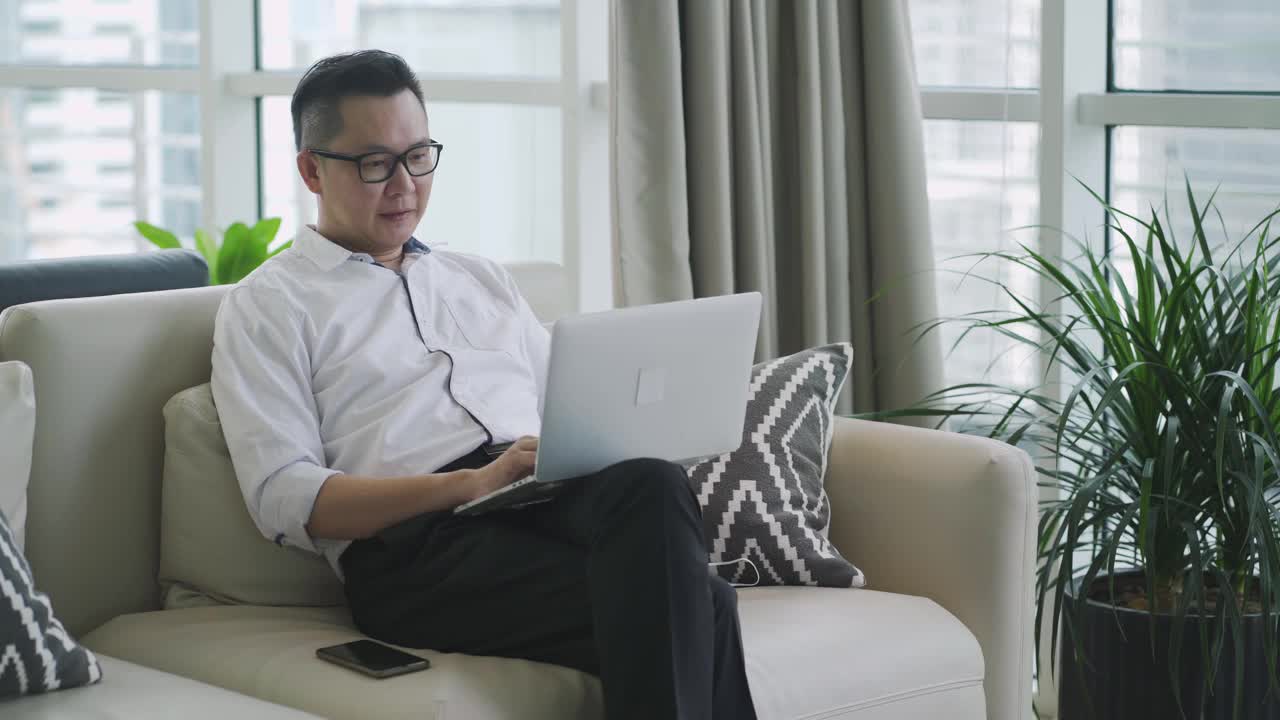 亚洲华人中年商人使用笔记本电脑坐在商务休息室微笑查看他的电话信息视频下载
