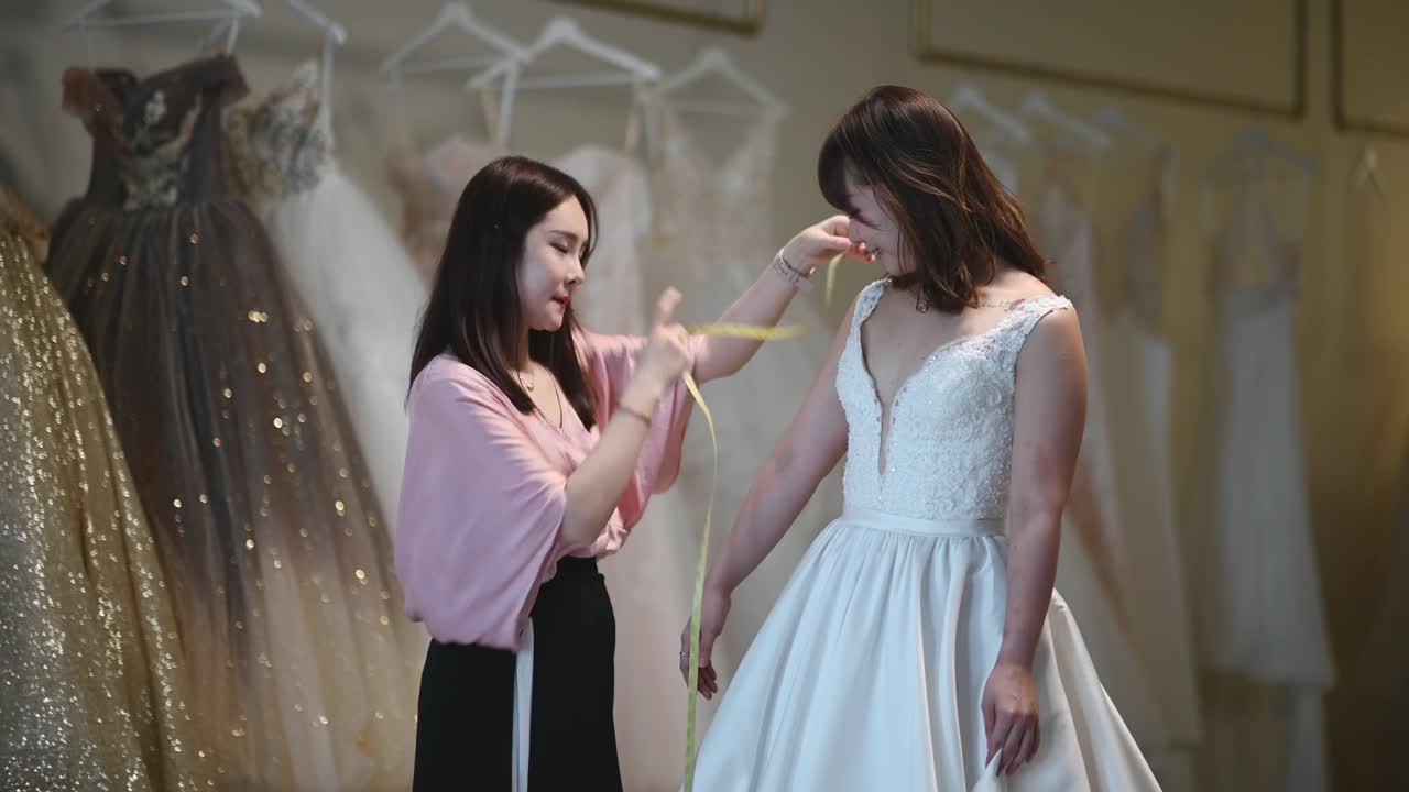 亚洲华人女婚纱店老板正在为顾客测量新娘的体型，为顾客量身定制婚纱视频素材