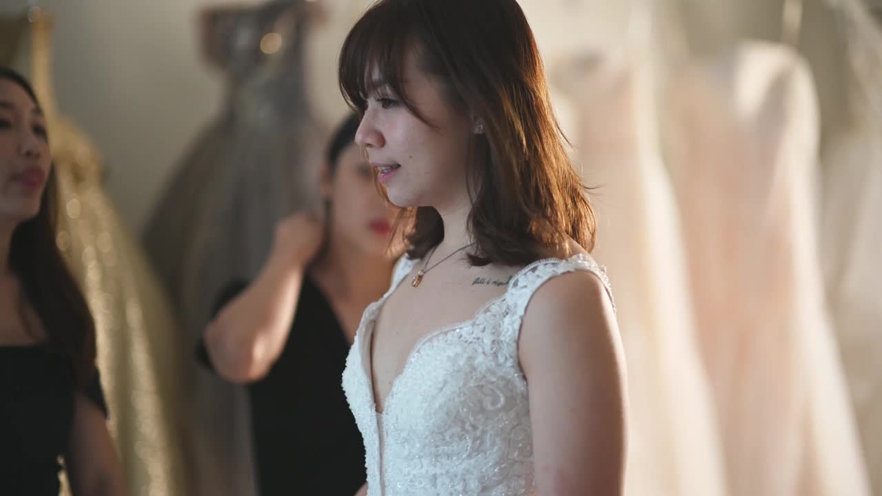 亚洲的中国新娘在婚纱店试穿婚纱，伴娘在旁边欣赏婚纱的美丽视频下载