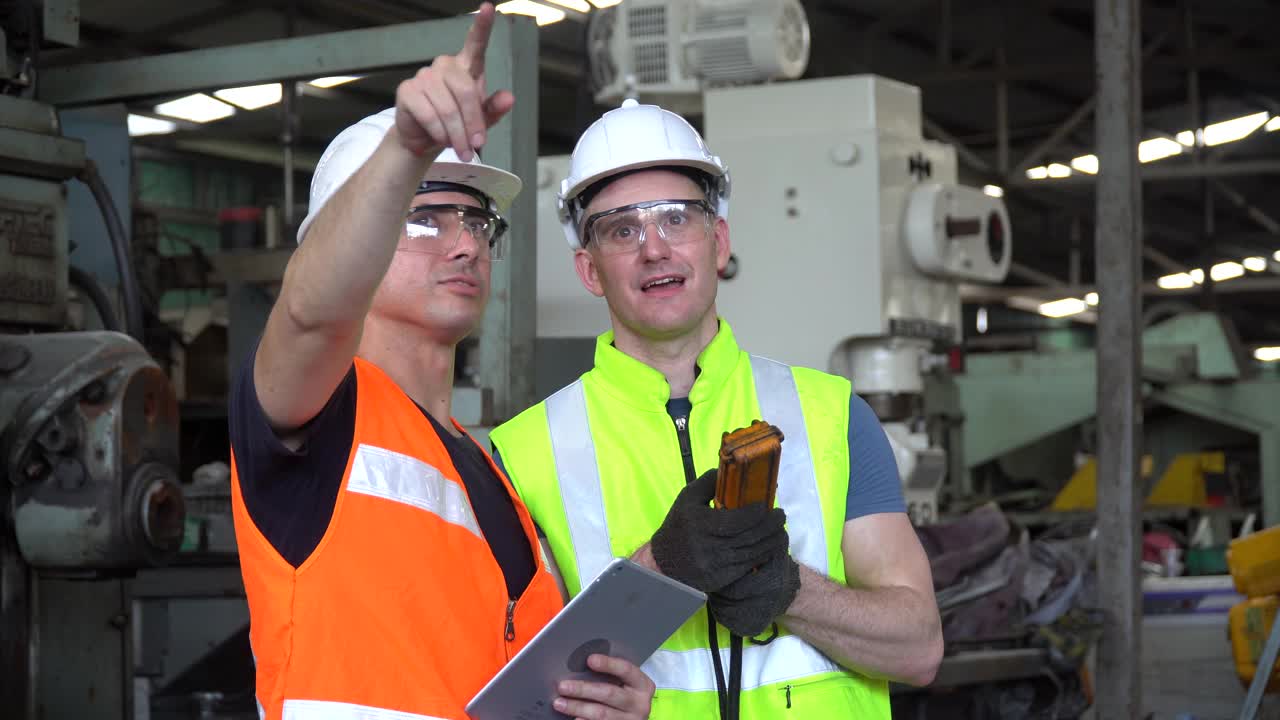 当工人们在工业工厂工作时，工程师和技术经理用平板电脑与重型机器远程控制交谈。视频下载