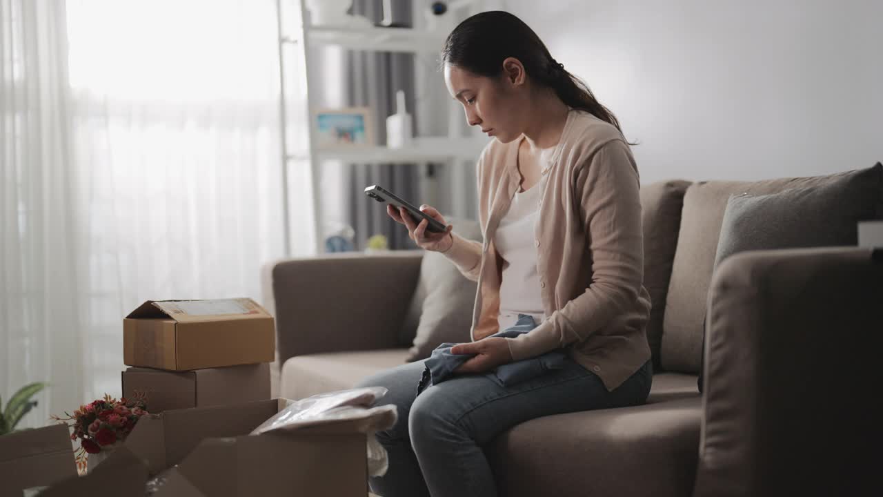 亚洲女人消费者觉得坐沙发不好，拿着电话与网店谈论家里订购的问题产品，打电话投诉。视频素材