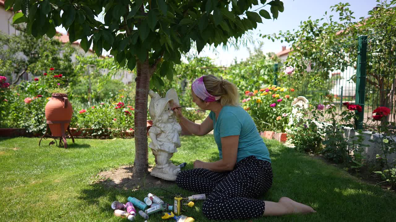 女艺术家在她的艺术花园侏儒雕像绘画户外。视频下载