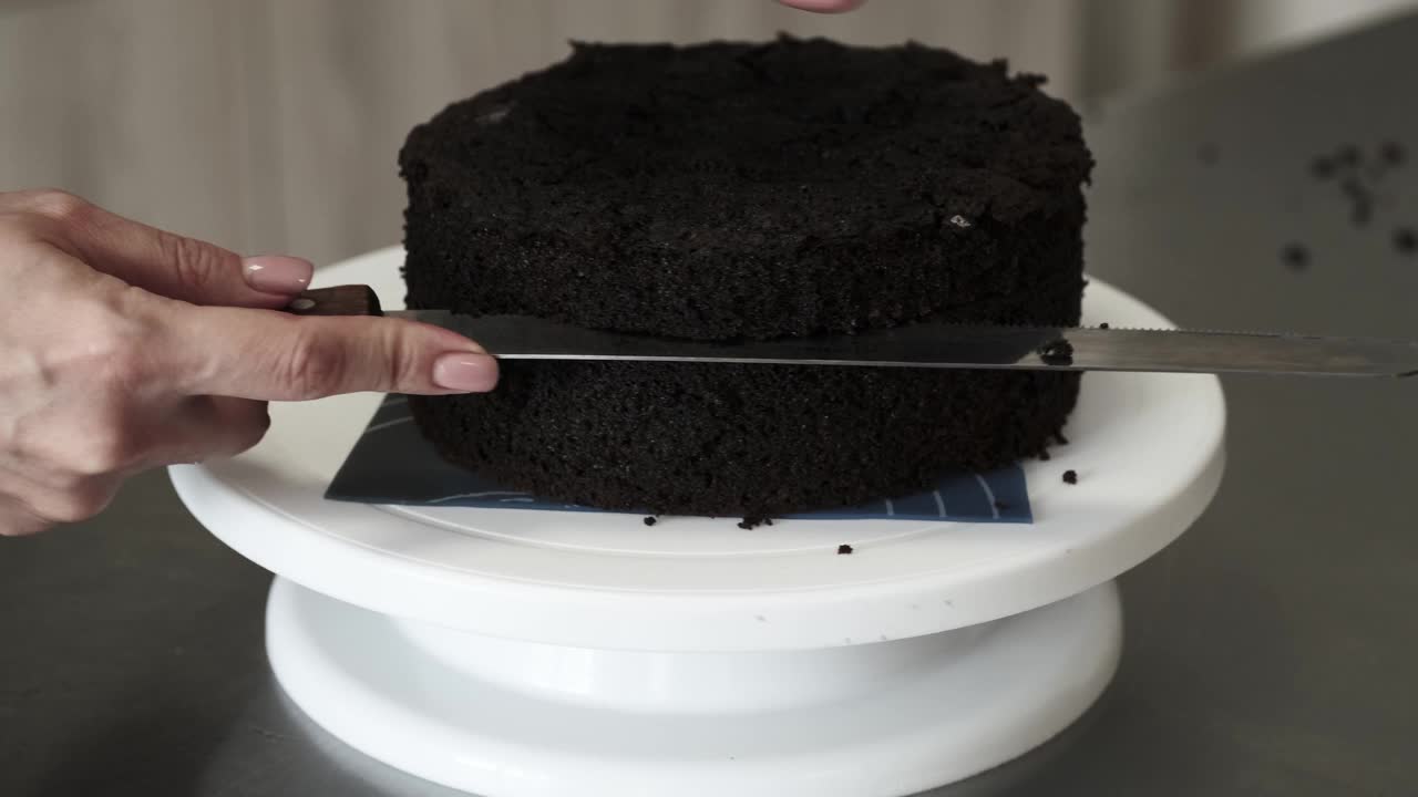 4K女糕点厨师用刀切巧克力海绵蛋糕，特写镜头。缓慢的运动。蛋糕制作过程。视频素材