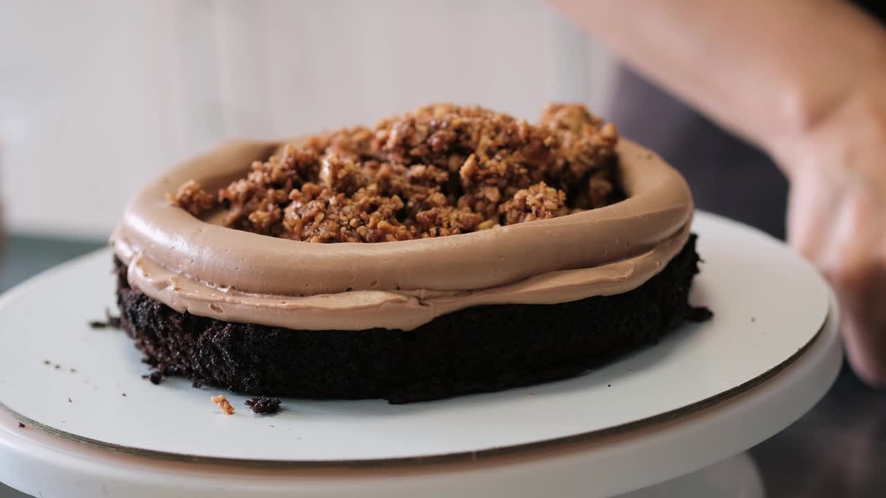 4K女糕点厨师把坚果馅放在巧克力海绵蛋糕上，特写镜头。缓慢的运动。蛋糕制作过程。视频素材