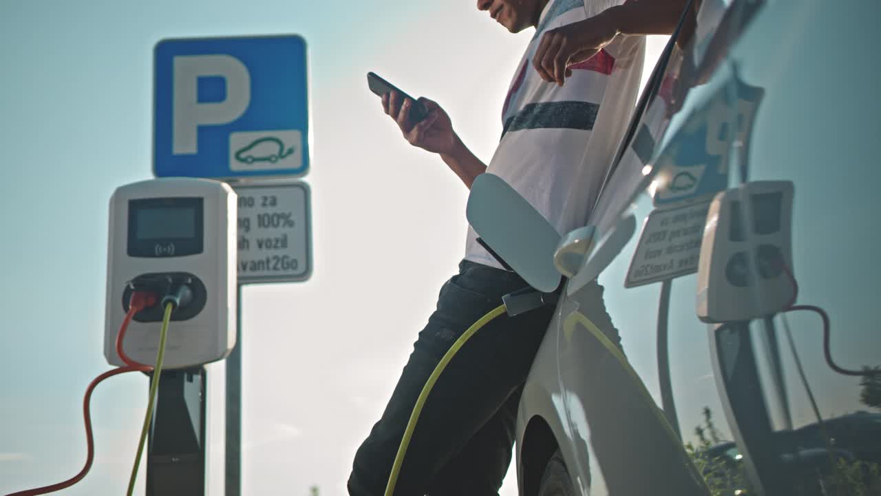 一名年轻人在停车场充电时使用智能手机视频素材