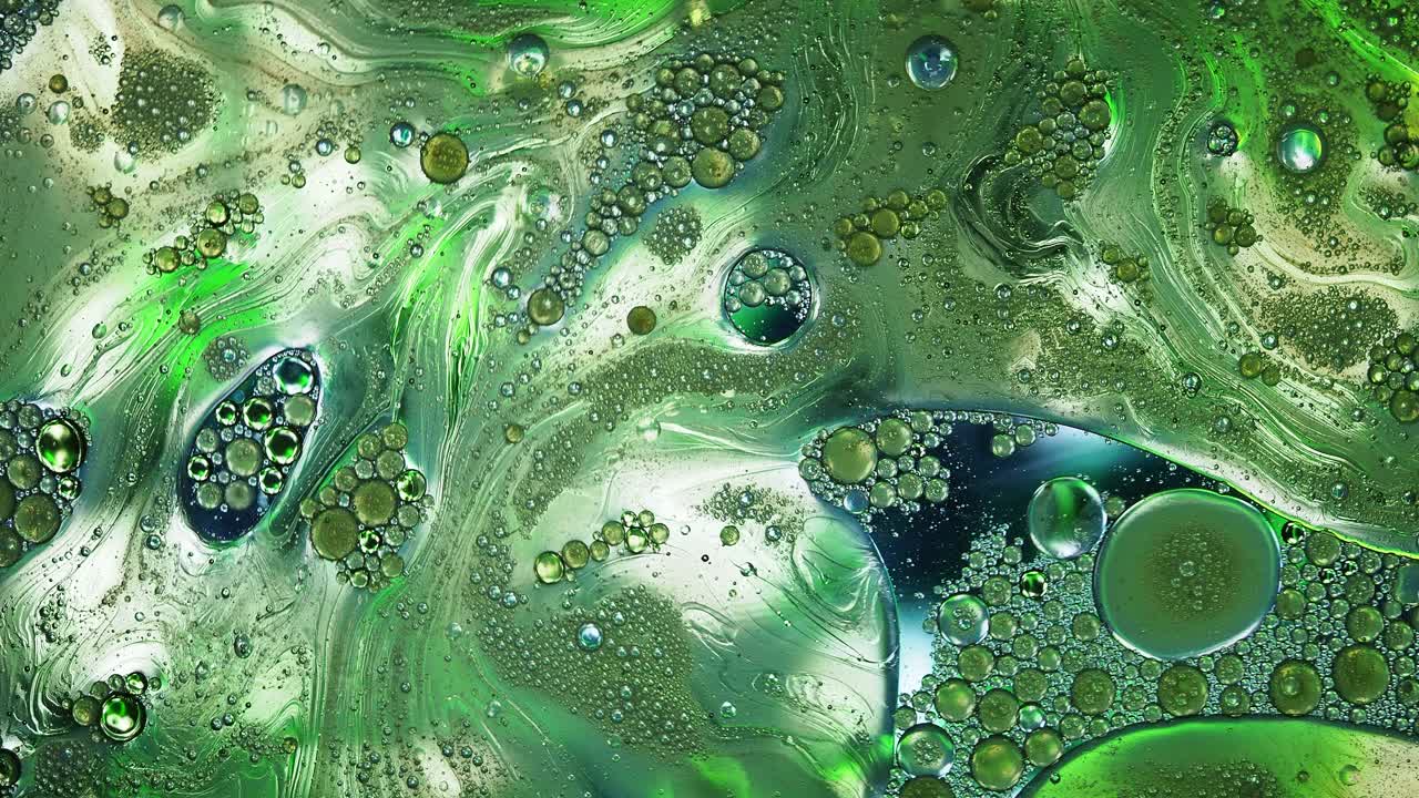 在绿色的背景上，混合液体和彩色颜料在运动。视频下载