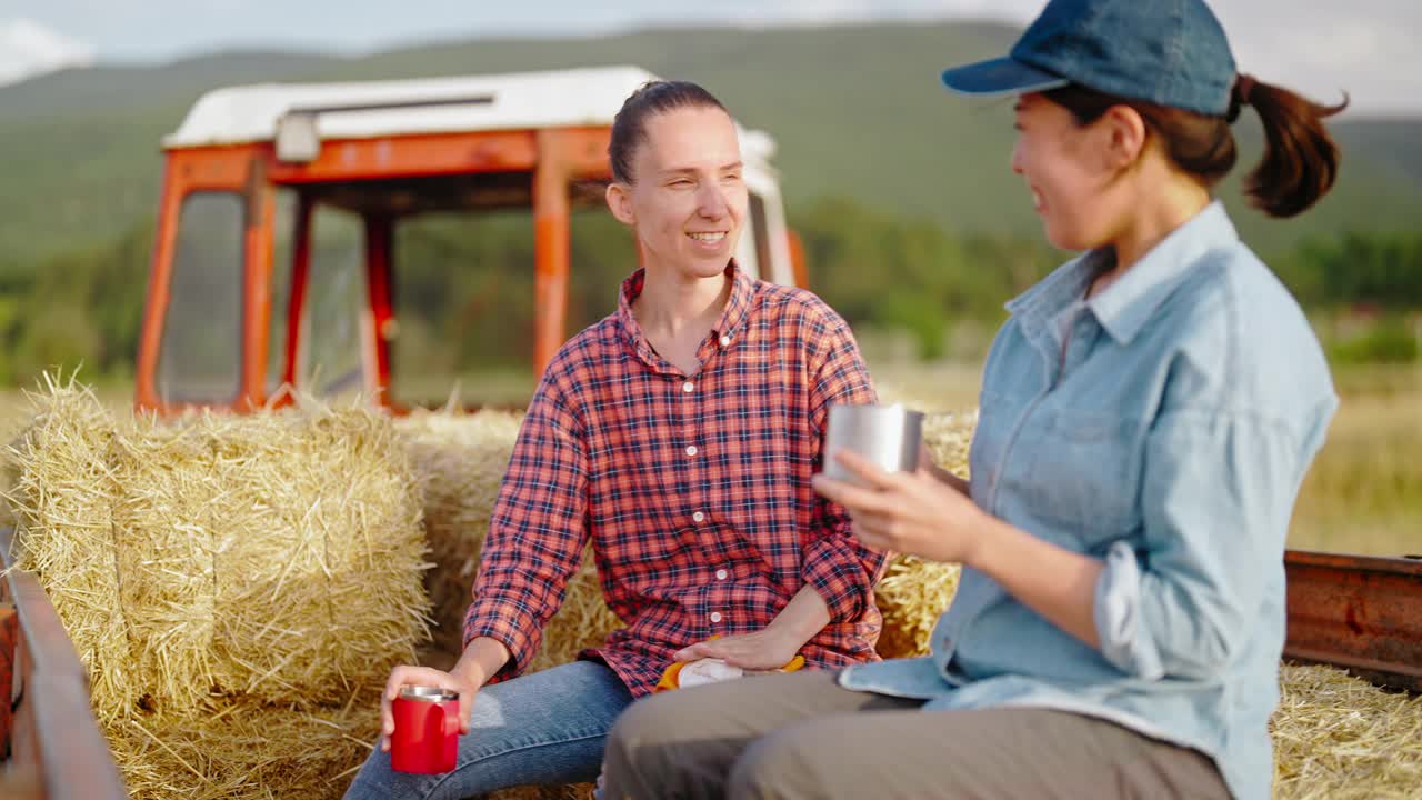 两个女农民在田间劳作，休息在拖拉机挂车上，互相交谈着视频下载