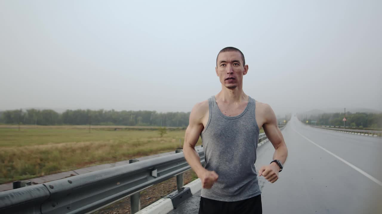 亚洲人的外表和运动员的身材在雨中跑步在潮湿的沥青路上，汽车经过，前面的景象。抱负和速度的概念视频素材