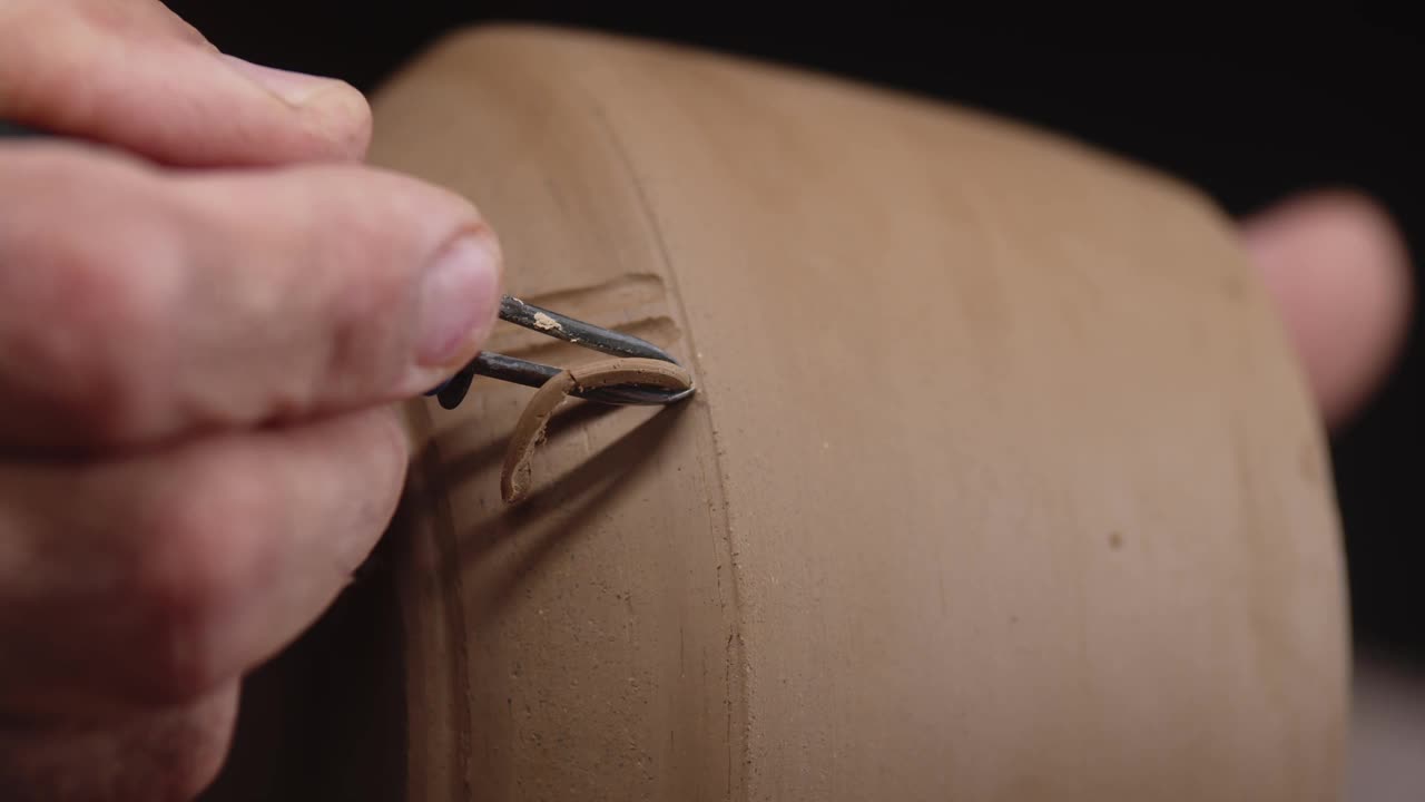 陶工的手用刮刀在光滑的黏土制品上剪出木棍形状的图案。宏射击视频素材