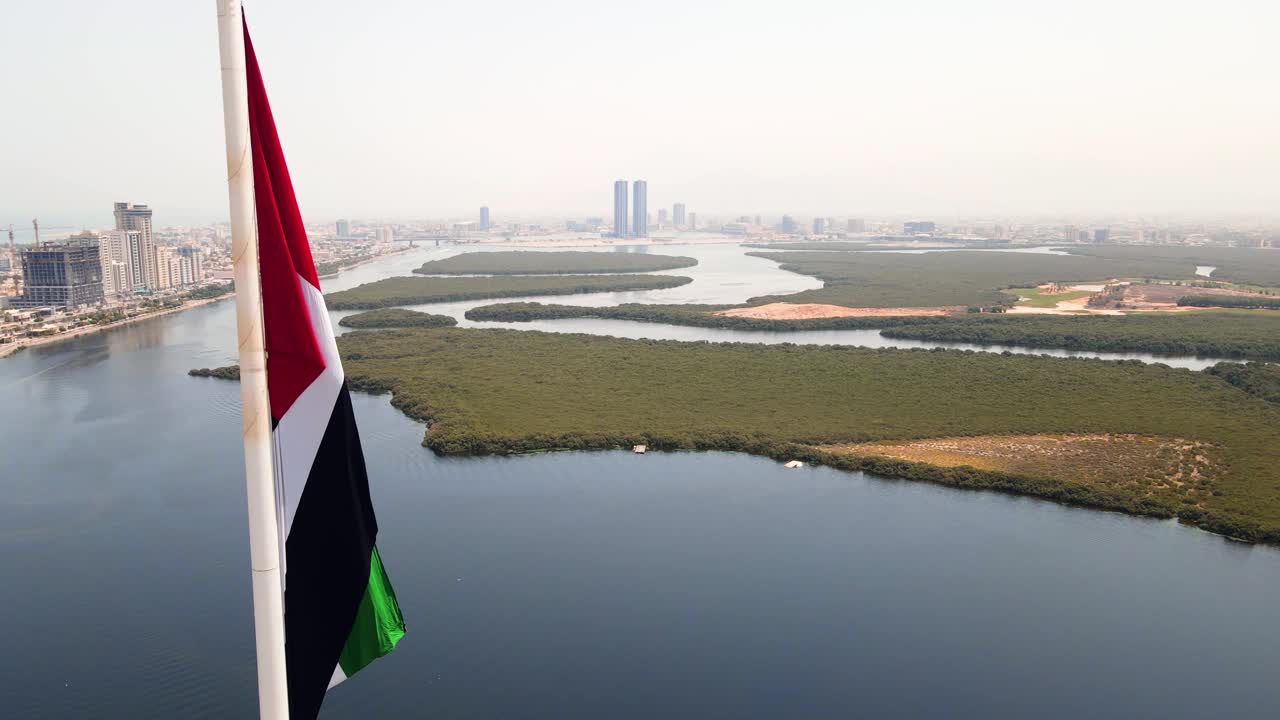 阿联酋国旗和Ras al Khaimah酋长国空中城市景观的标志性天际线上升在阿联酋北部的红树林和小溪视频下载