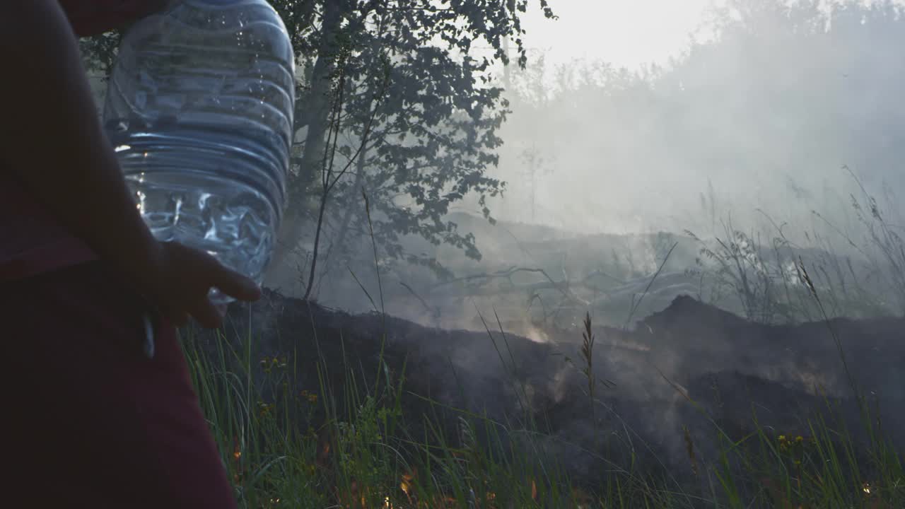 一个志愿的男人或男孩扑灭一场野火。用塑料瓶倒水。雨林野火灾害，干燥灌木丛燃烧，火灾原因。视频素材