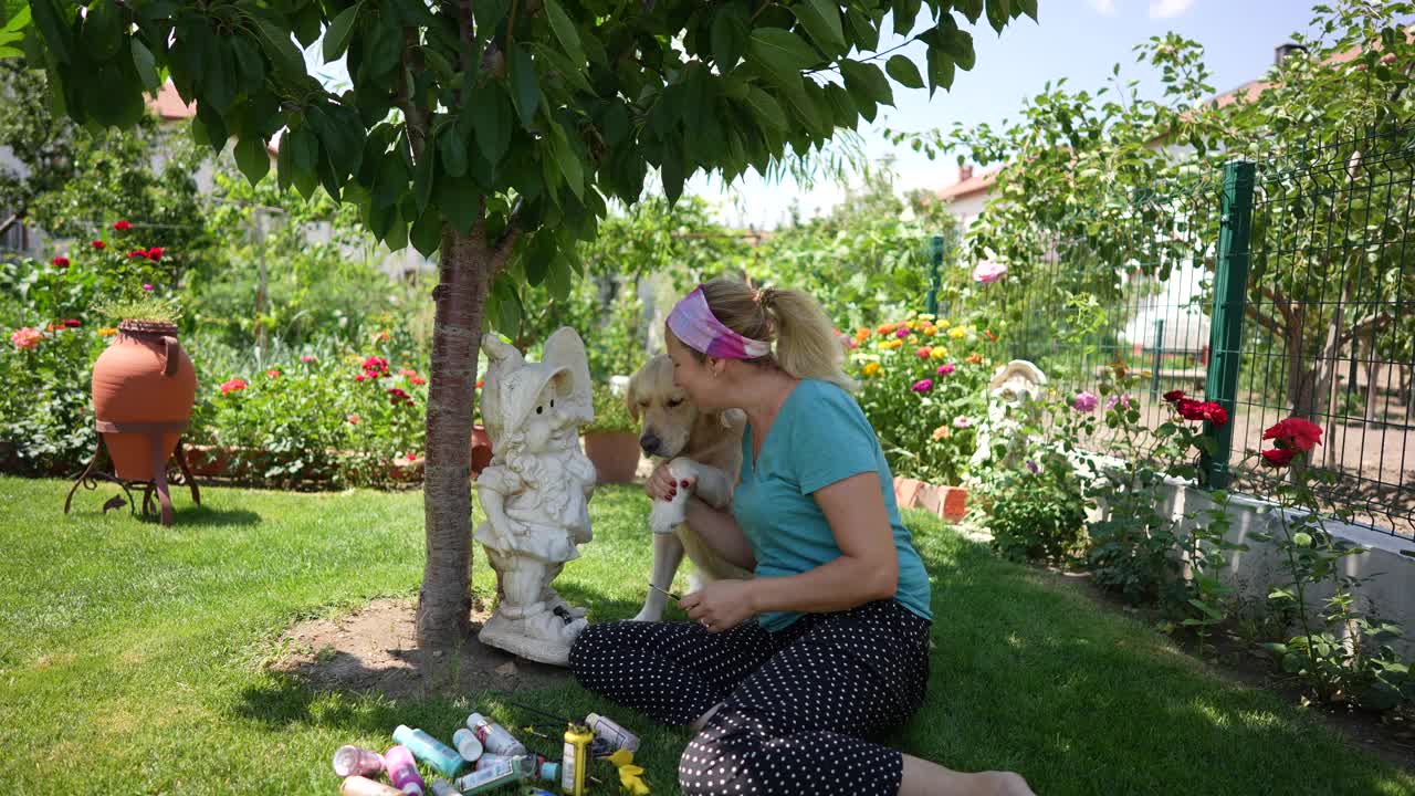 女艺术家在她的艺术花园侏儒雕像上工作，在她的花园与金毛猎犬户外绘画。视频下载