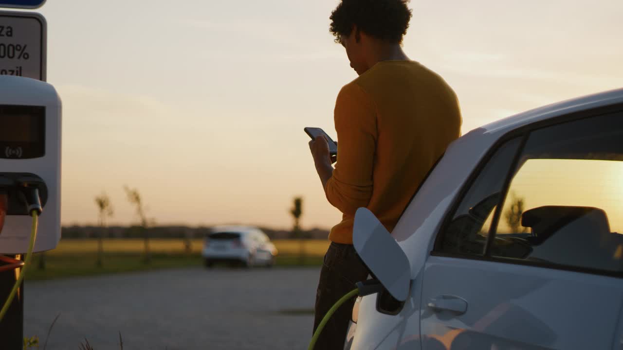 日落时分，一名年轻的黑白混血男子在停车场给他的电动汽车充电视频下载