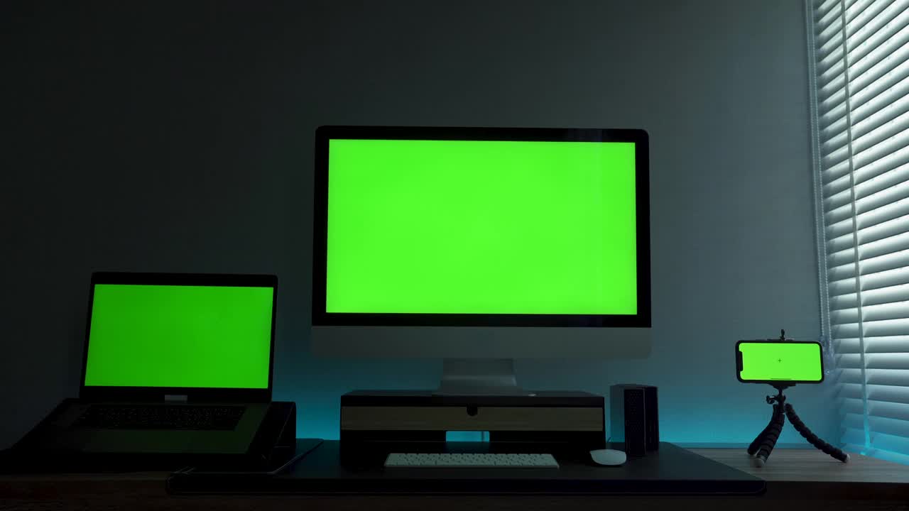 客厅的书桌上放着显示绿色色度按键屏幕的笔记本电脑和智能手机。视频下载