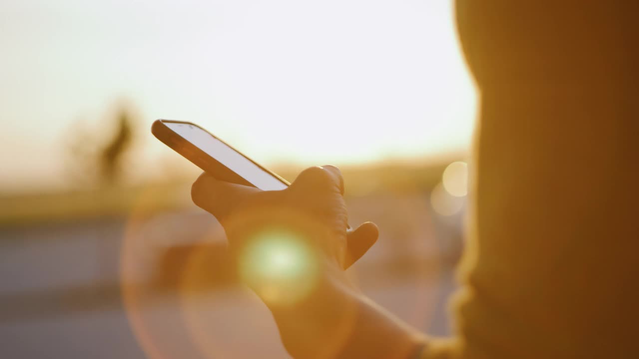 日落时分，一名年轻人在停车场使用智能手机视频下载
