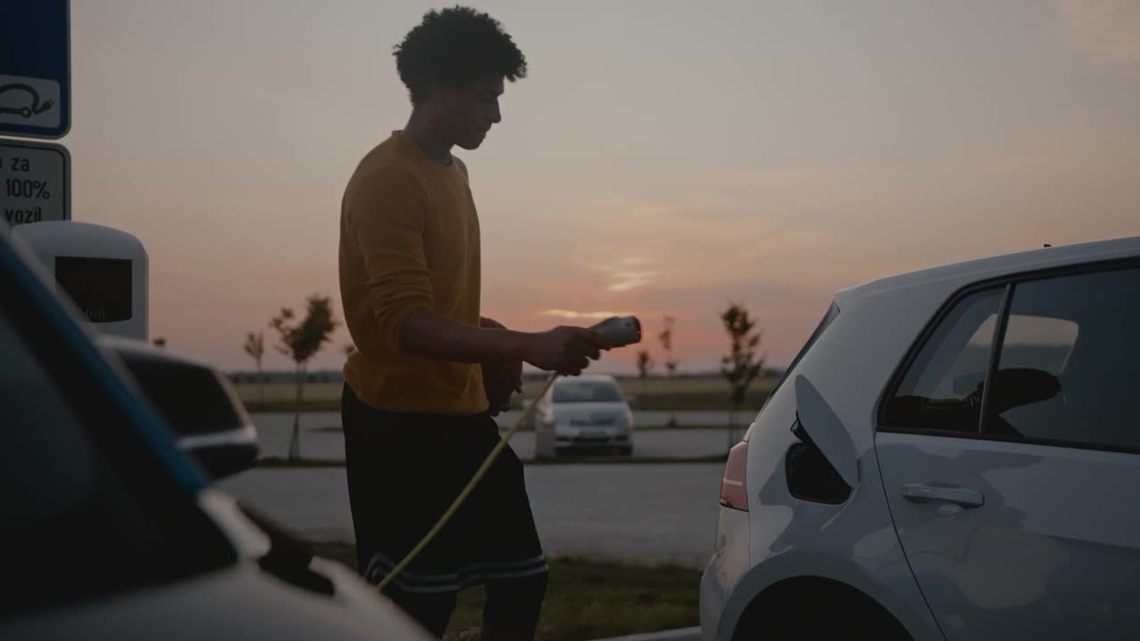 黄昏时分，年轻的篮球运动员在停车场给他的电动汽车充电视频下载
