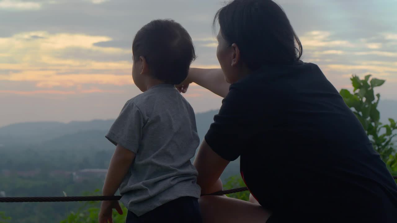 日落时幸福家庭的背面，亚洲母亲和17个月大的儿子在山上自由地看大自然，在一起，教孩子可持续发展，在自然中的幸福概念。视频素材