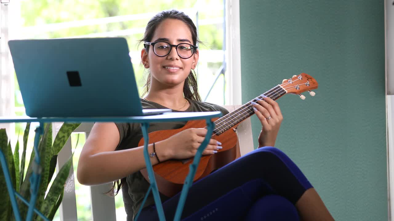年轻女子在家里弹吉他和使用笔记本电脑视频下载
