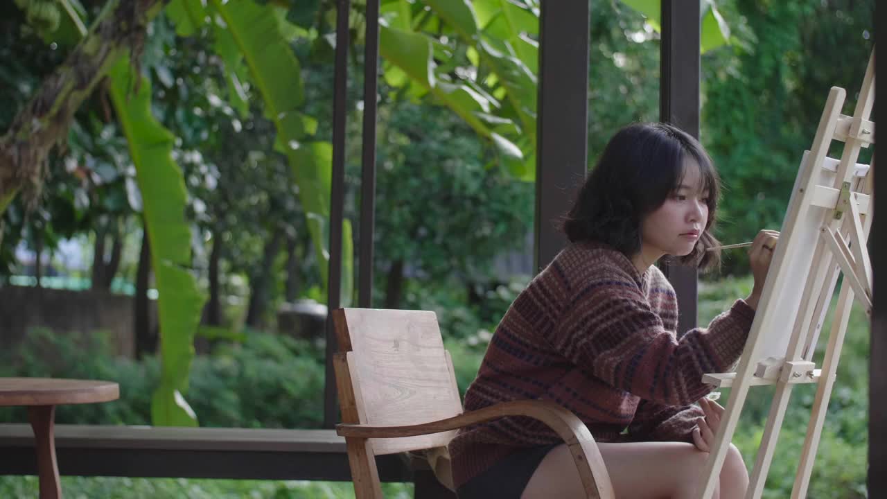 年轻的亚洲女性艺术家用画笔和画架绘画。视频素材