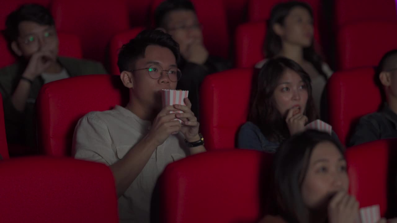 一名亚洲中国年轻人把爆米花倒向其他观众，吓了一跳视频素材