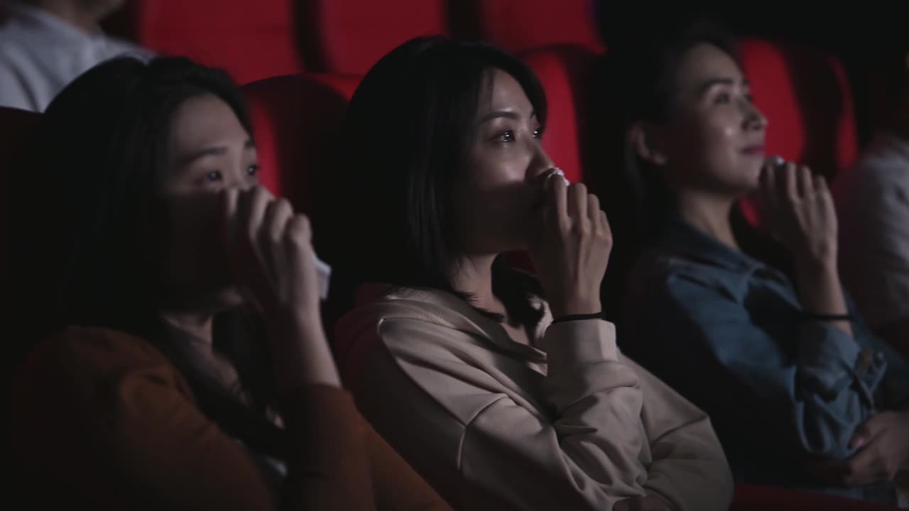 亚洲的中国女人在电影院看感伤的电影，在电影院用纸巾擦眼泪视频下载