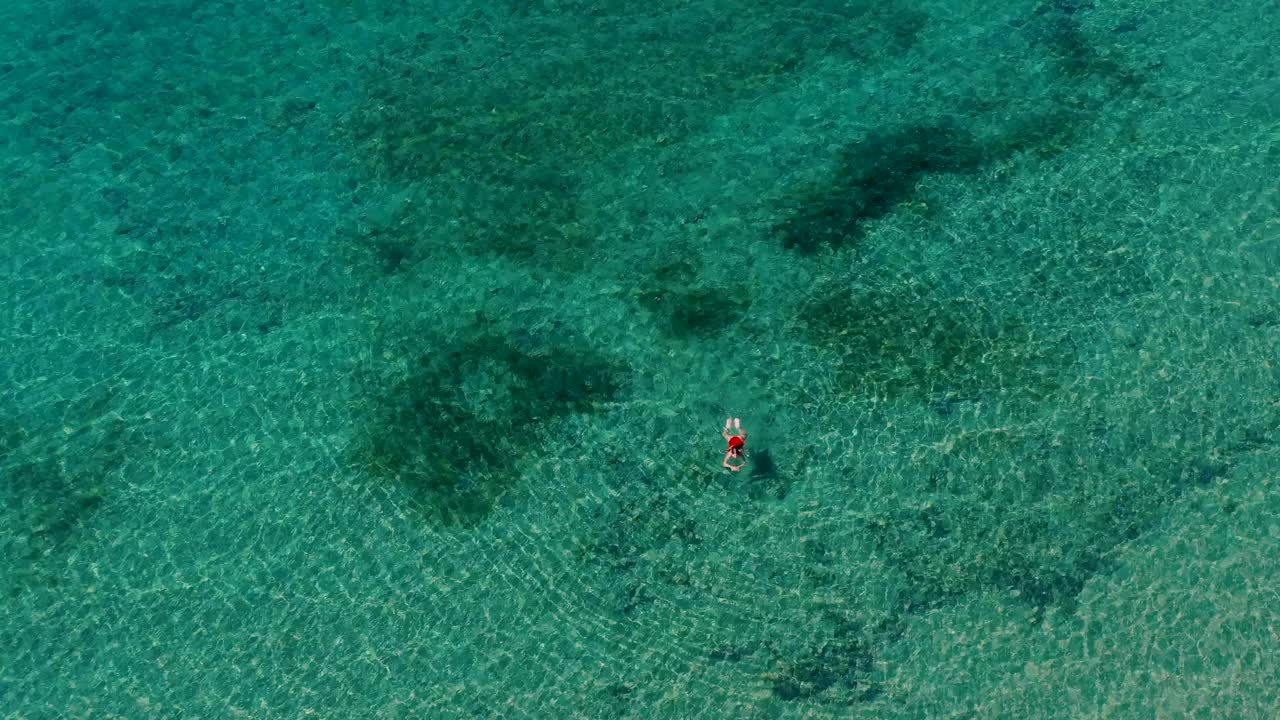 鸟瞰图，一个女人穿着红色泳衣独自游泳在蓝绿色的海视频下载