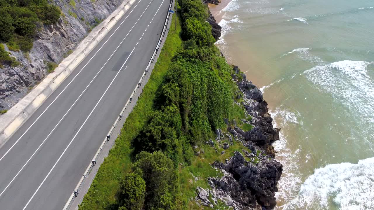 当车辆经过时，无人机在道路上方飞行。在西班牙坎塔布里亚的Oriñón海滩上视频下载