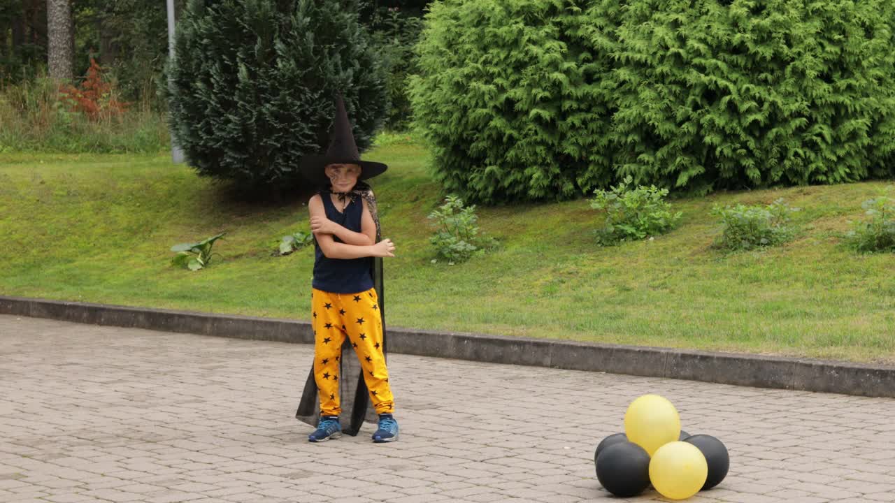 万圣节跳舞的男孩。穿着狂欢节服装的少年在户外。一名男生正在玩橙色和黑色的气球。视频素材