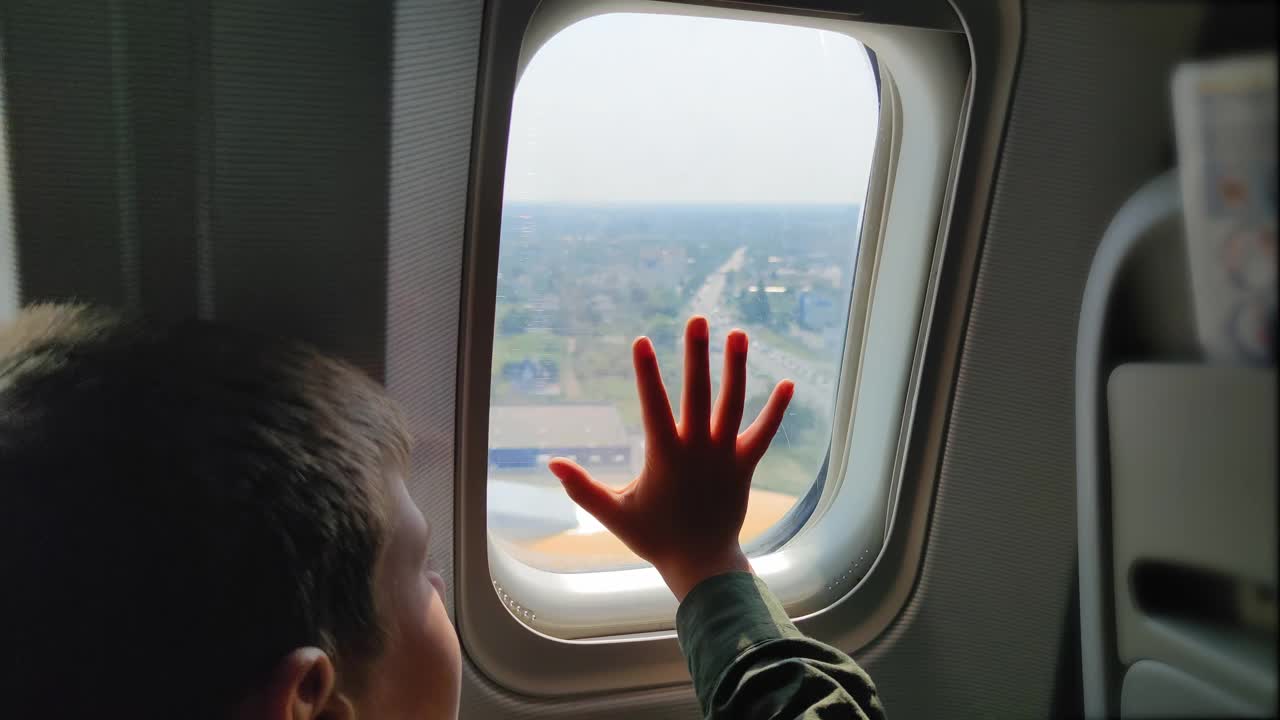 到达机场时，小男孩在飞机着陆时把手放在窗户上，饶有兴趣地看着风景视频下载