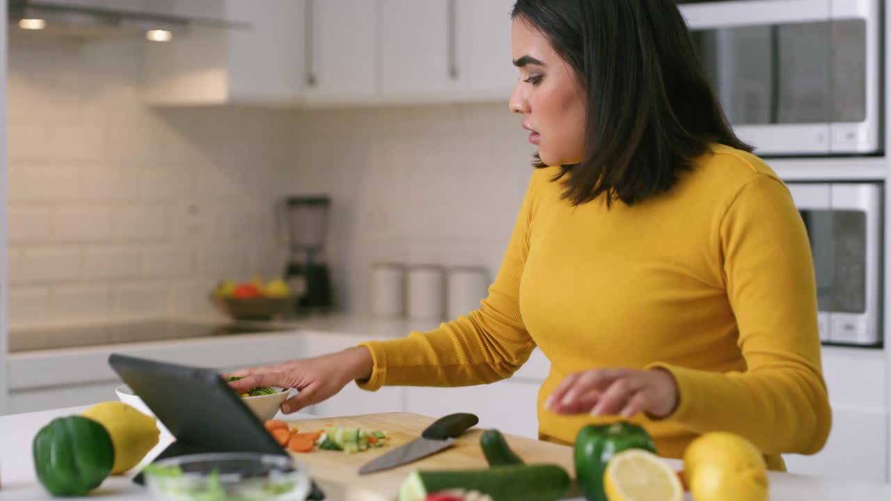 一段4k视频显示，一名年轻女子在家里用数码平板电脑做健康食品时看起来很紧张视频下载
