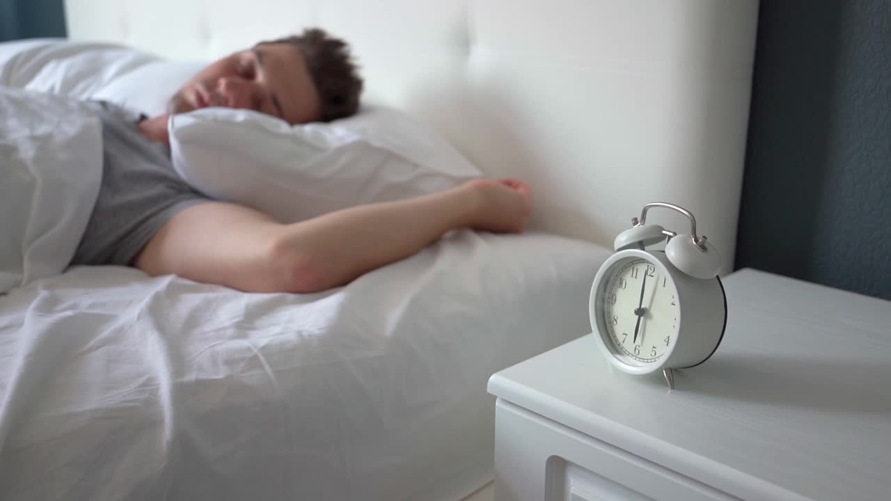 早上按时早起。正在睡觉的男人不情愿地在警报中醒来视频素材
