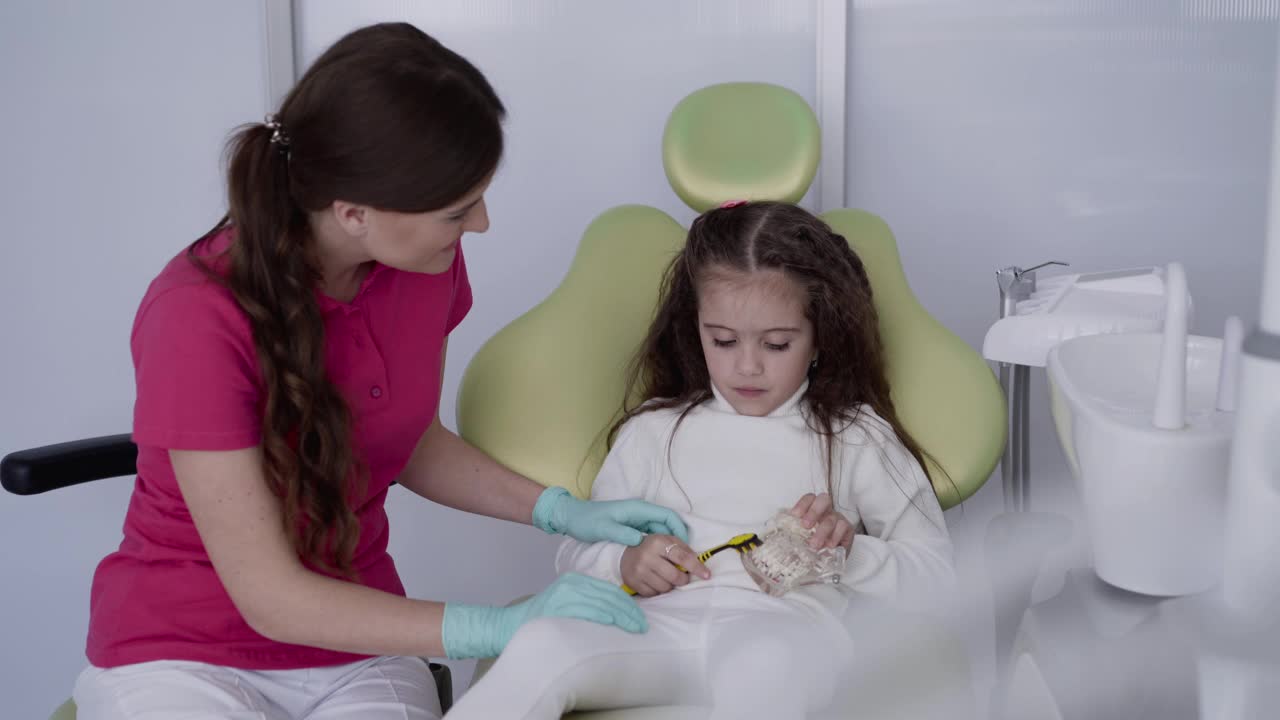在牙科医生用牙刷和下颌模型训练正确刷牙的女孩视频素材