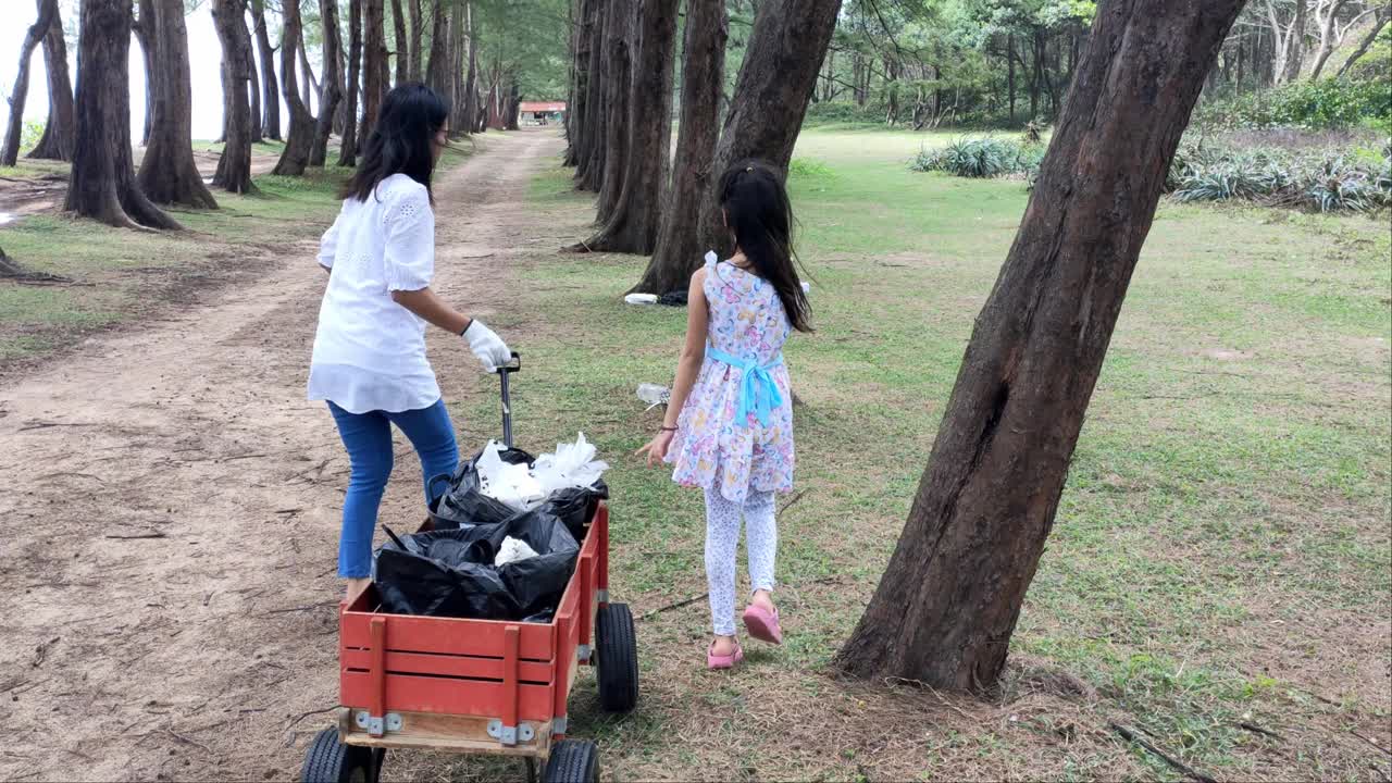 亚洲的母亲和女儿们坐在轮椅上把垃圾扔进海滩公园，以适当地限制垃圾。视频素材