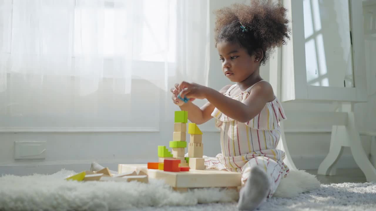 非洲女儿在客厅里玩木块玩具堆得最高，躺在地毯上心情愉快，笑着、笑着。幼儿园概念，低角度视角。视频下载
