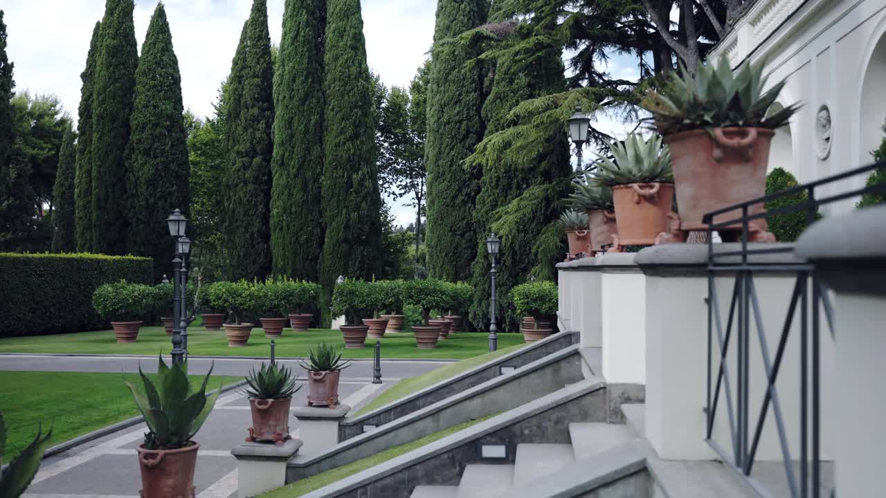 历史悠久的住宅物业，带有私人花园庭院，白色的古宫环绕着雄伟的常青树在天空的背景。巨大的砖棕色花瓶上生长着柠檬树，在别墅宫殿附近的绿色草地上，大理石楼梯视频下载