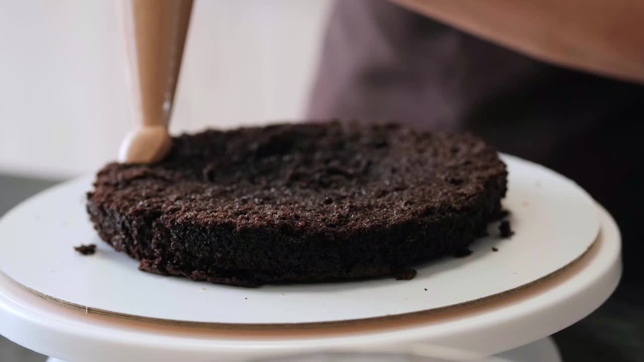 4K女糕点厨师用糕点袋将巧克力奶油涂在巧克力海绵蛋糕上，特写镜头。缓慢的运动。蛋糕制作过程。视频素材