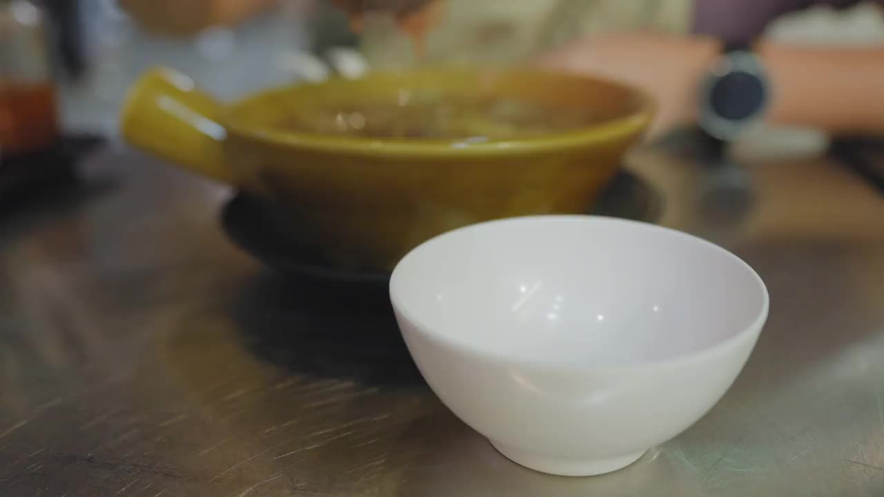 在曼谷唐人街耀拉瓦的一家街头小吃店里，大家在金属桌子上用塑料勺盛着热腾腾的鱼肚汤。女人用黑胡椒调味视频下载
