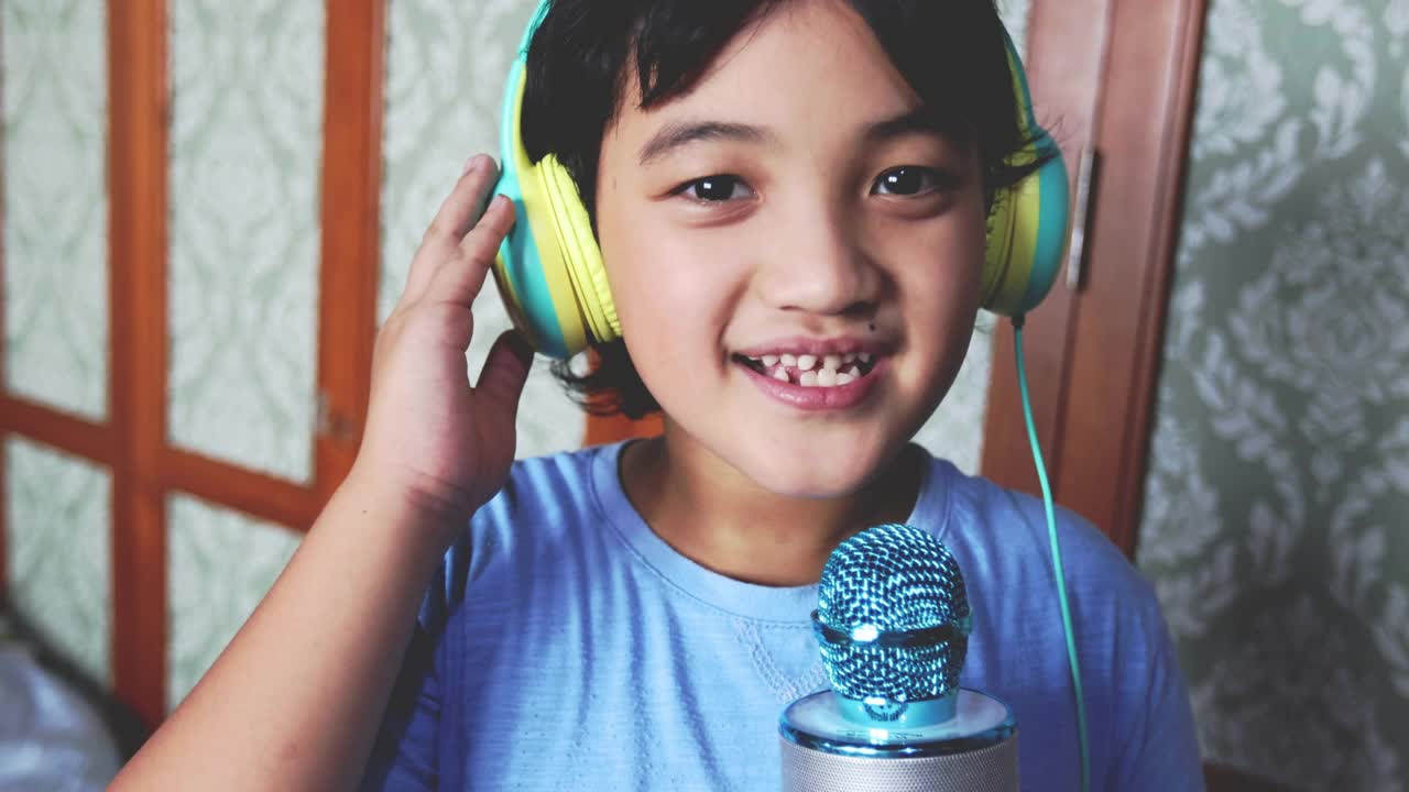 4K Footage亚洲泰国男孩在客厅用麦克风和耳机唱卡拉ok，穿着蓝色t恤。在家享受简单的快乐。放松时间，学习时间，呆在家里。视频下载