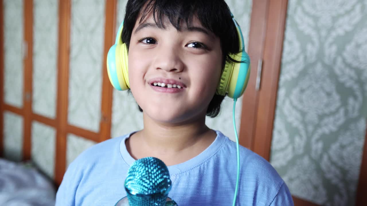 4K Footage亚洲泰国男孩在客厅用麦克风和耳机唱卡拉ok，穿着蓝色t恤。在家享受简单的快乐。放松时间，学习时间，呆在家里。视频素材