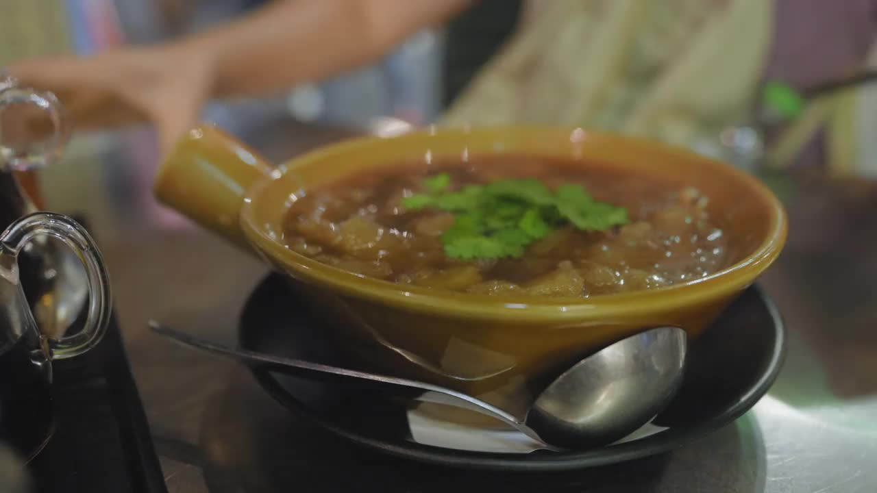 在曼谷唐人街耀拉瓦的一家街头小吃店，在金属桌子上的碗里端上热腾腾的鱼肚汤。女人调整桌子准备吃饭视频下载